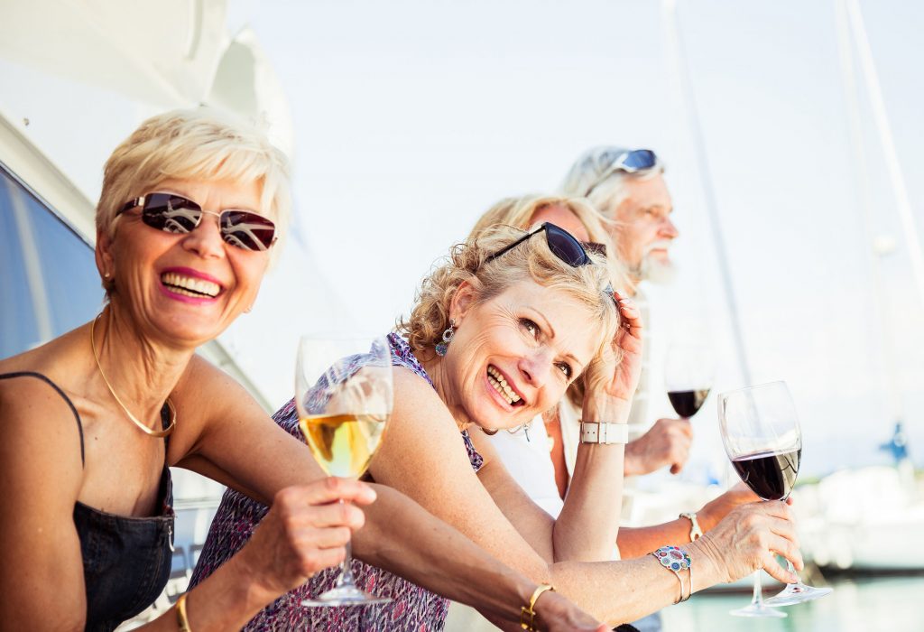Four people smiling and holding glasses of wine while relaxing on a boat during a sunny day.