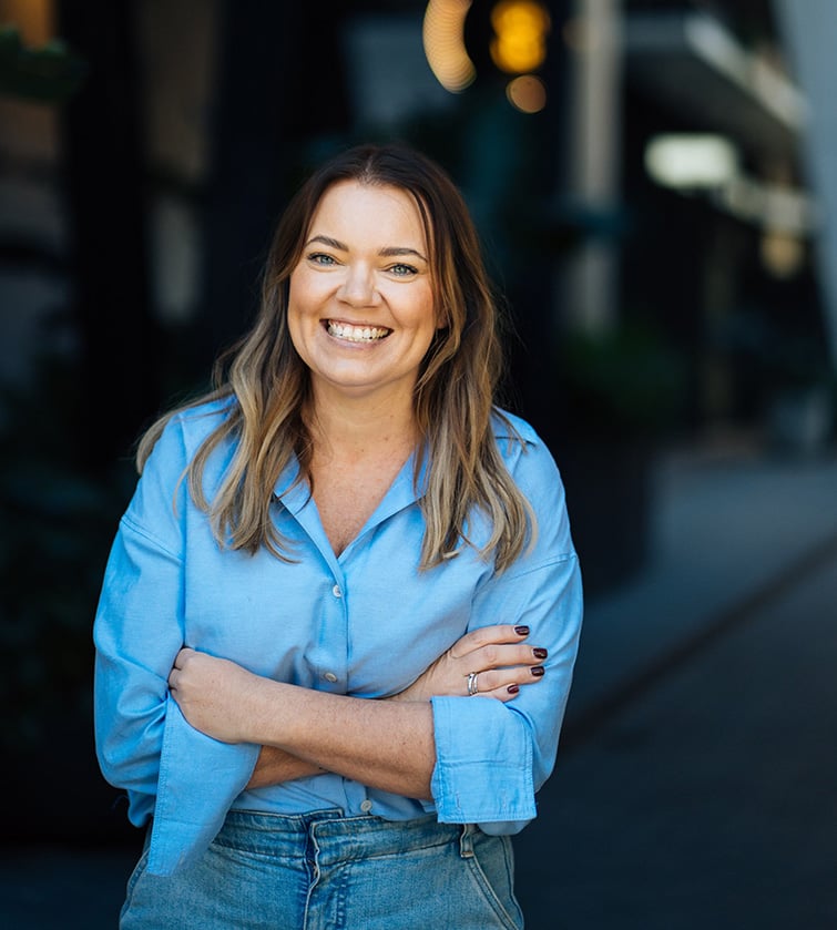A medium-shot portrait of Michelle wearing a light blue button-down shirt and denim jeans