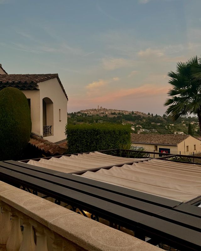 A view from a balcony overlooking a Mediterranean landscape at sunset, featuring a terracotta-roofed villa.