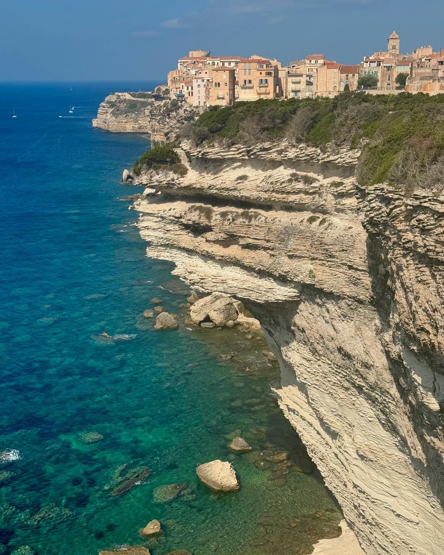 A scenic view from a grassy cliffside overlooking white limestone cliffs and a historic town perched on the edge