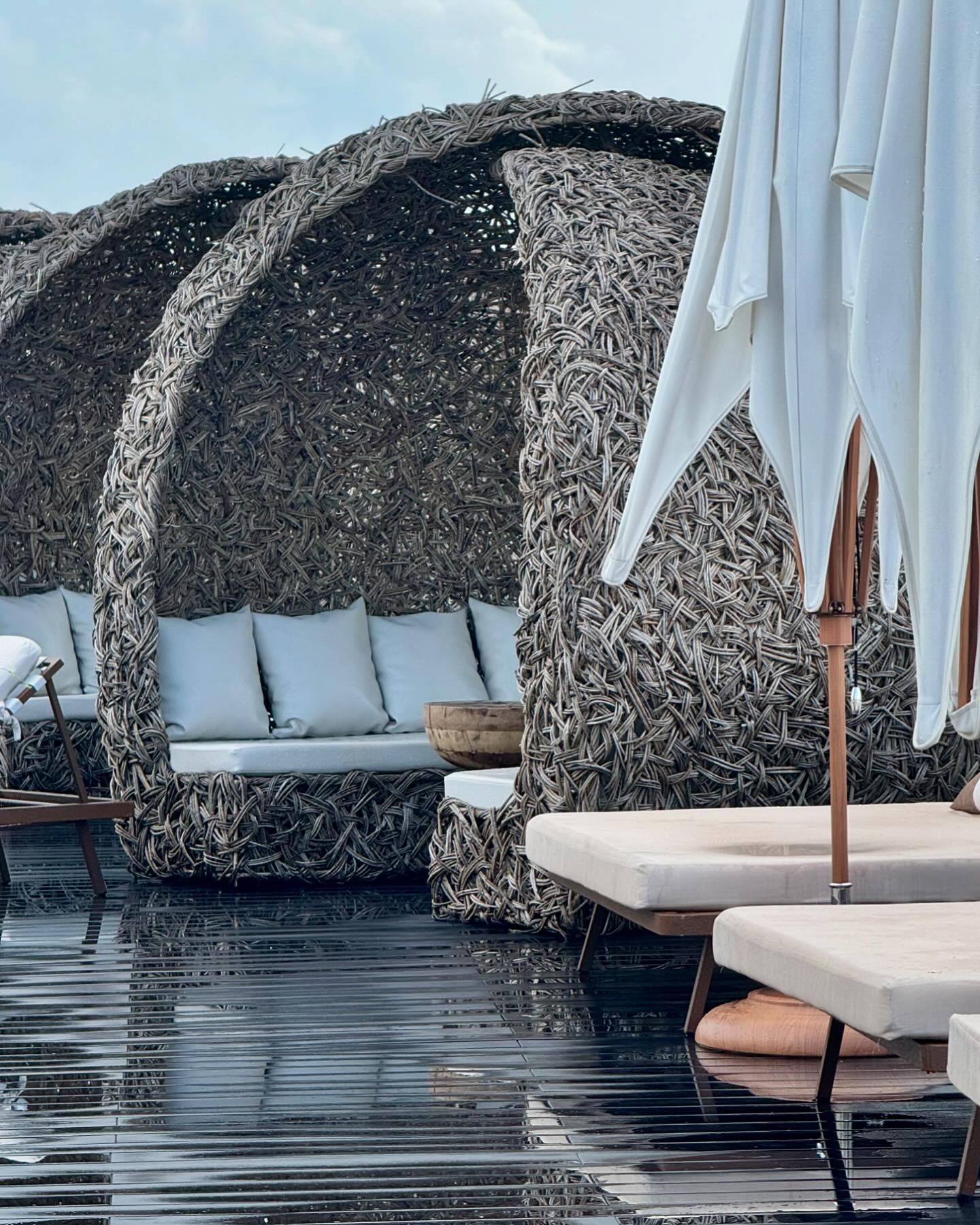 A luxurious poolside lounge area with woven, nest-like cabanas and white-cushioned sun loungers