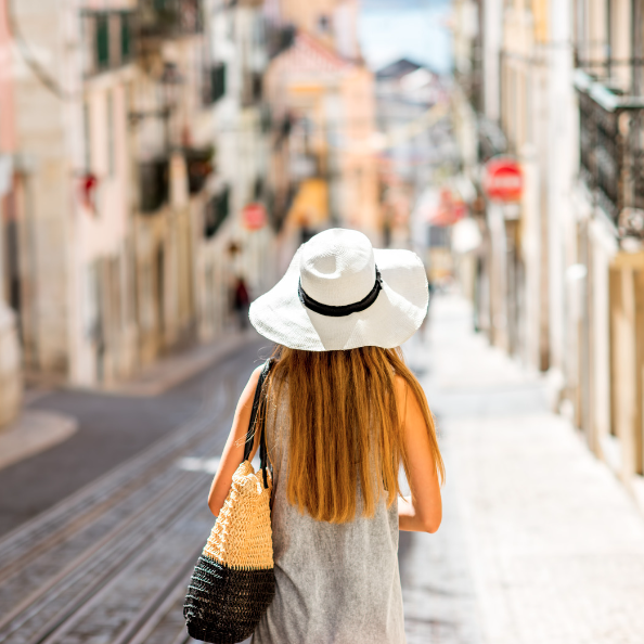 A woman with long blonde hair wears a white sun hat and carries a straw tote bag