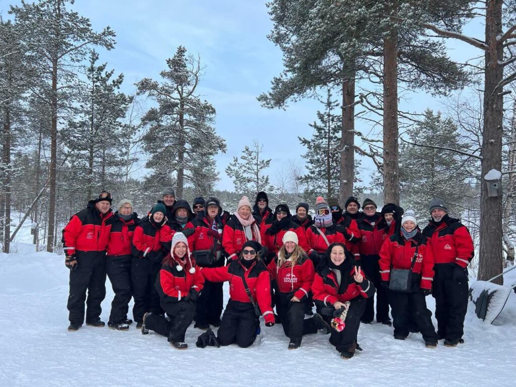 A large group of people wearing matching red and black parkas pose for a group photo